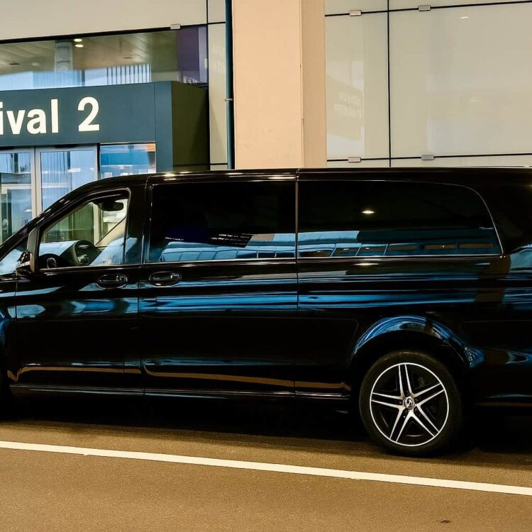 Black luxury van parked at airport arrival zone, ready for passenger pickup, showcasing professional transportation services by Globetransporte GmbH.