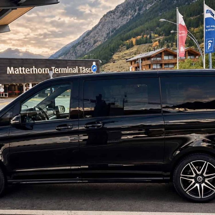 Black Mercedes-Benz V-Class 250 by Globetransporte at Täsch Station near Zermatt, ready for a private transfer to Lech am Arlberg, Austria.
