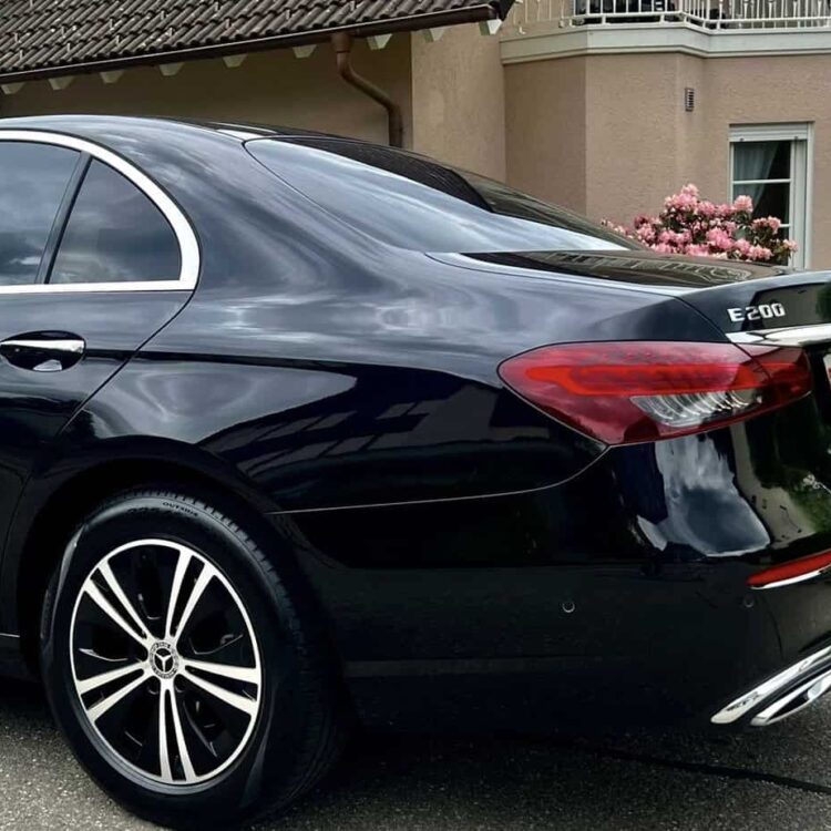Luxury black Mercedes-Benz E200 sedan parked on residential street, showcasing elegant design and premium features, ideal for executive transportation and chauffeur services.