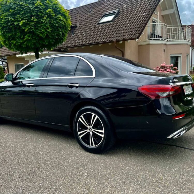 Elegant black sedan parked on a residential street with well-maintained houses and lush greenery in the background.