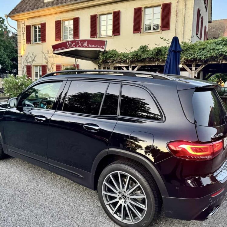 Black Mercedes-Benz GLC 250 SUV parked in front of a traditional Swiss hotel and restaurant, highlighting luxury car transportation services by Globetransporte GmbH.