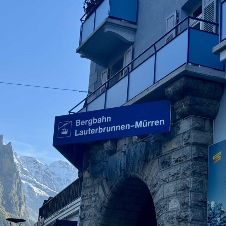 Mountain cable car sign for Lauterbrunnen-Mürren at Bergbahn station, Switzerland, with scenic mountain backdrop.
