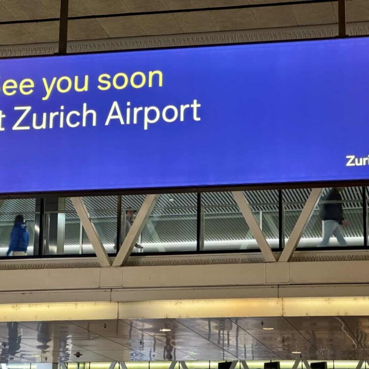 Travel sign at Zurich Airport with a message "See you soon at Zurich Airport" on a large digital display.
