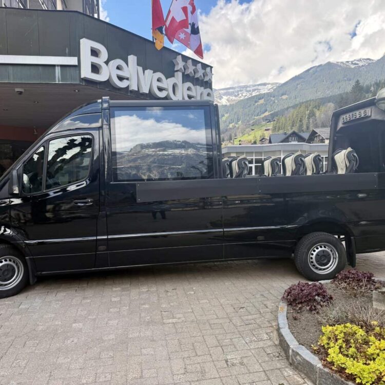 Transport van parked outside Belvedere hotel in Switzerland, used for passenger and luggage transportation, with scenic mountain background.