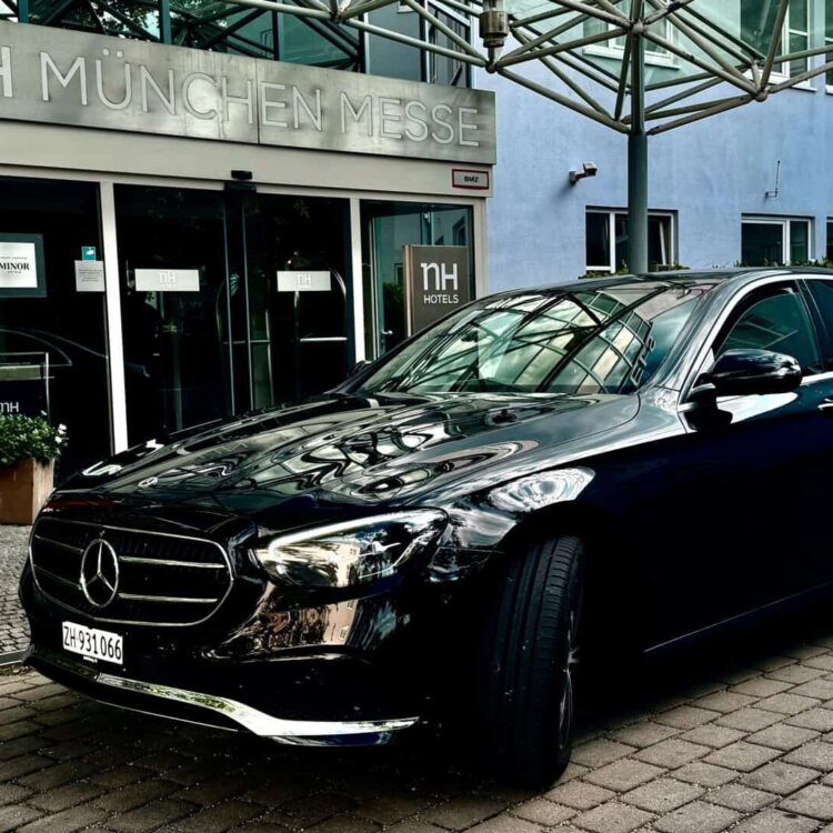 Black Mercedes-Benz sedan parked outside NH München Messe hotel in Munich, Germany.